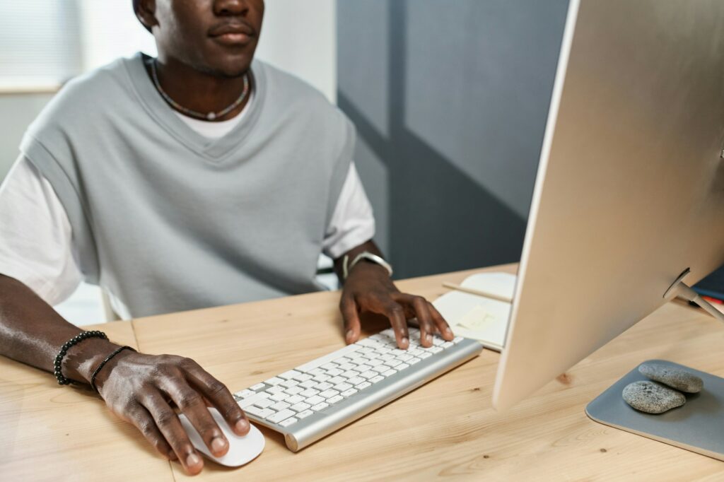 Close-up of young black man in t-shirt clicking on mouse and pressing button