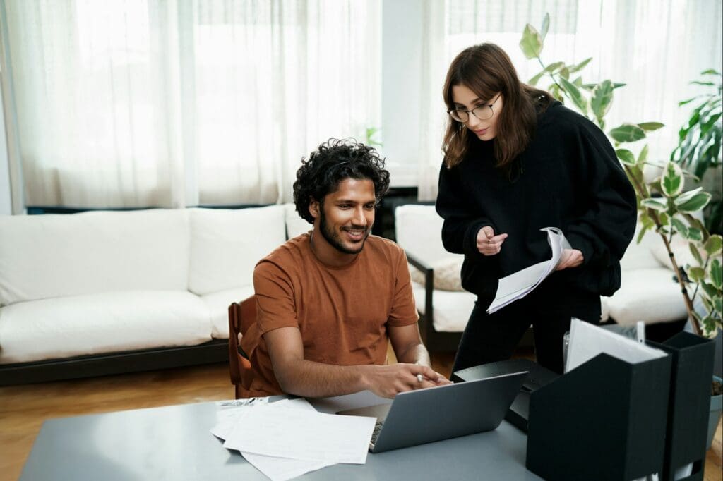 Diverse students working together: girl referring to papers, guy on a laptop