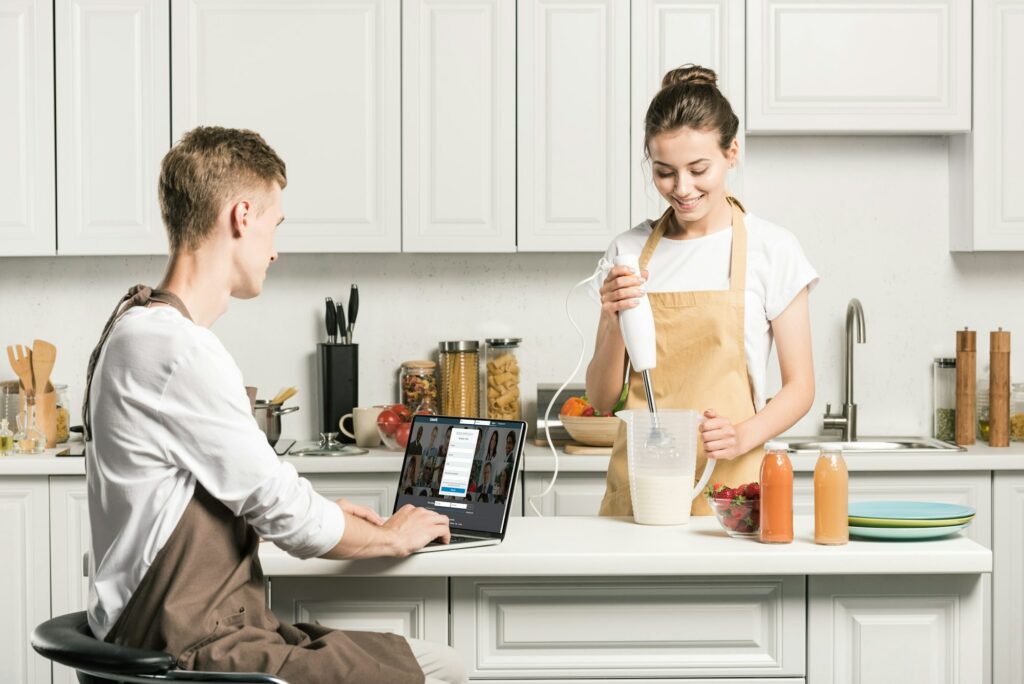 girlfriend cooking and boyfriend using laptop with loaded linkedin page in kitchen