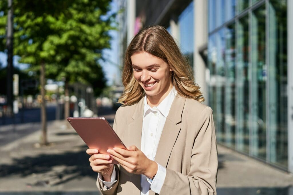 Portrait of happy businesswoman smiling, holding digital tablet on street near office building