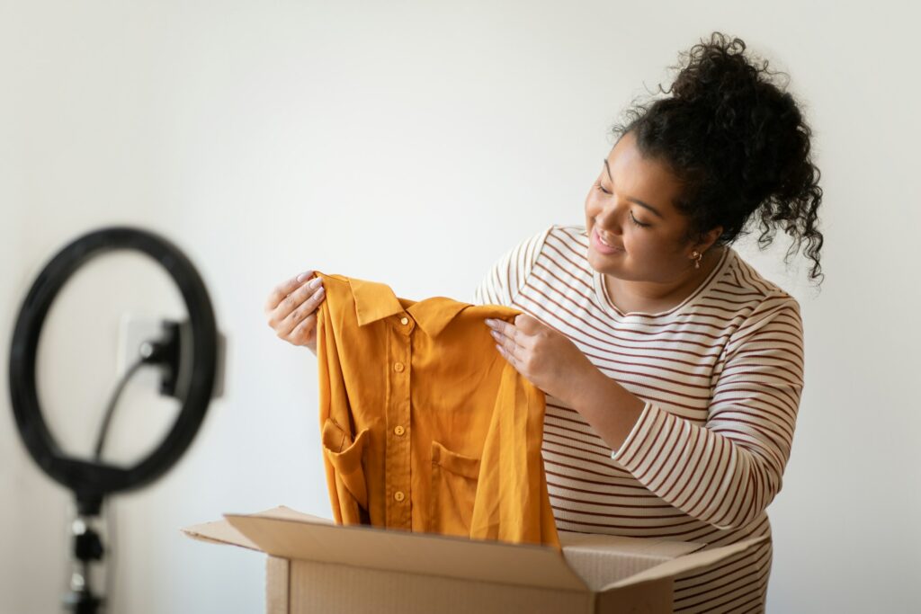 Positive chubby woman fashion blogger showing brand clothes, unpacking parcel