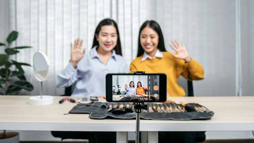 Two beauty blogger waving hands with audience on smartphone while recording.