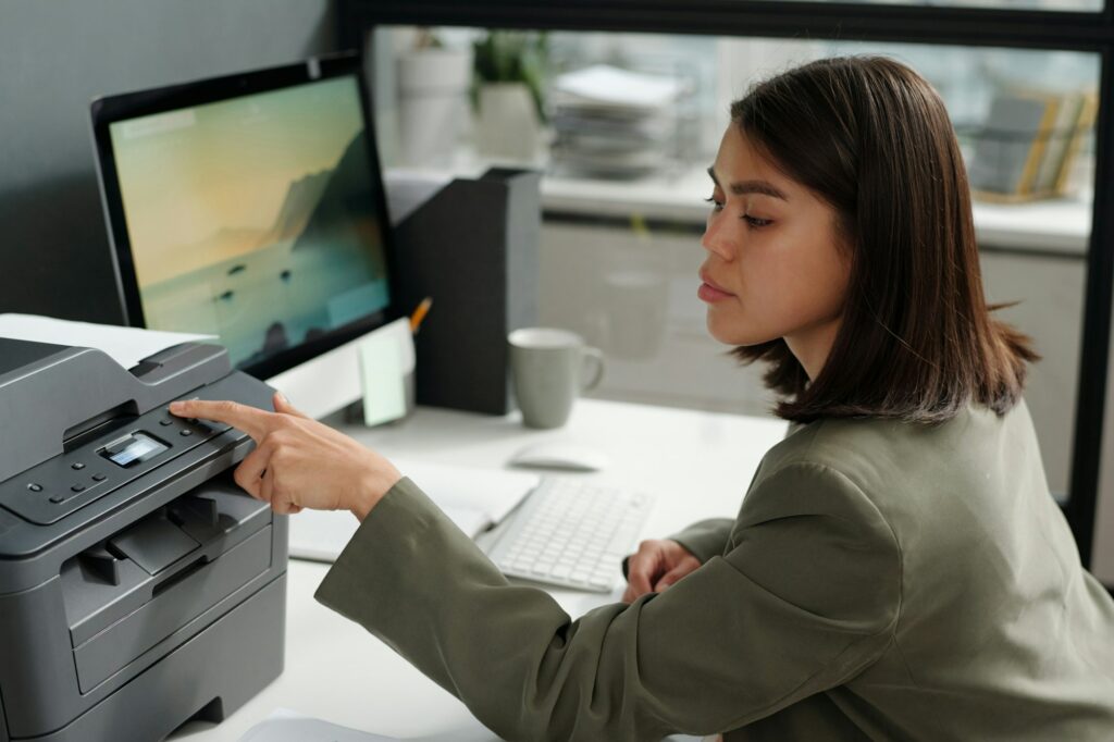 Young confident businesswoman pressing button on panel of xerox machine
