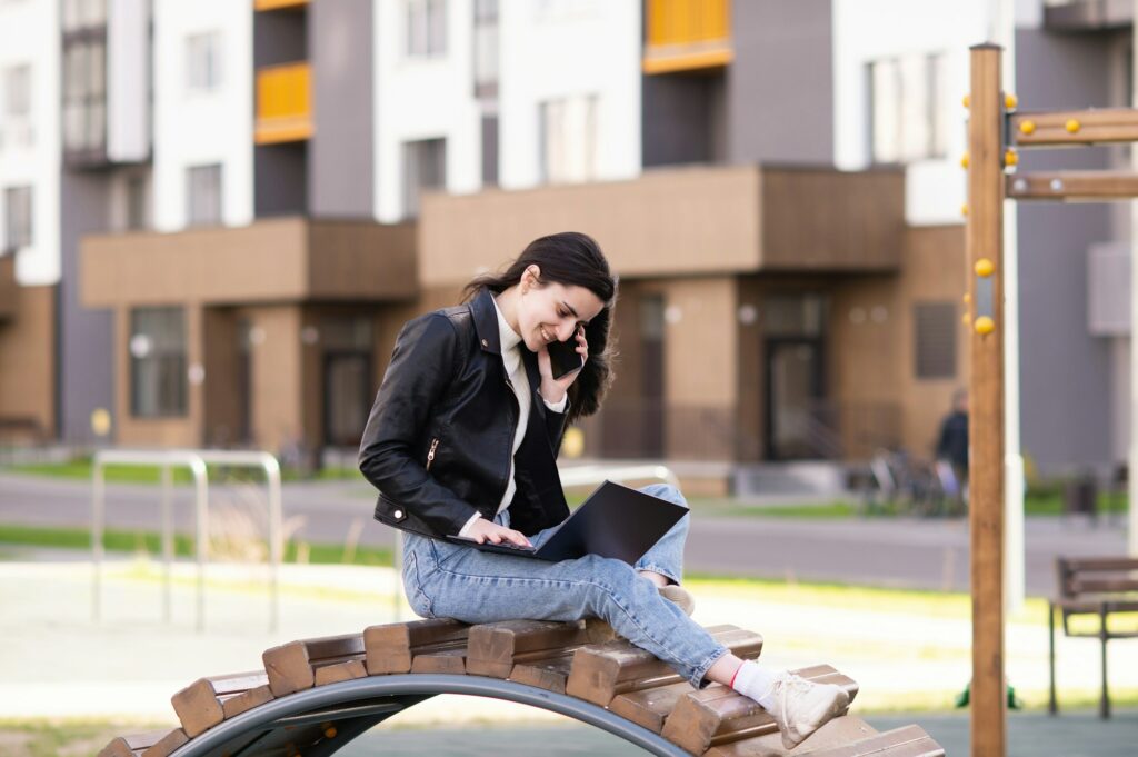 A young girl from the marketing field is talking on the phone, working in her laptop on the street