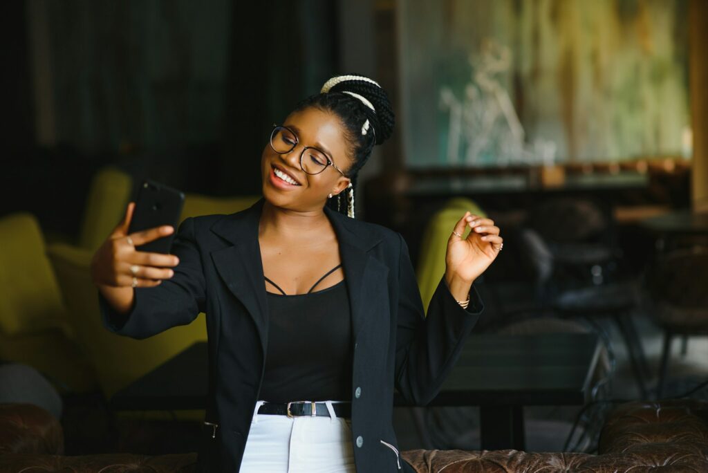 Cheerful dark skinned woman in trendy wear and spectacleson cafe posing for picture