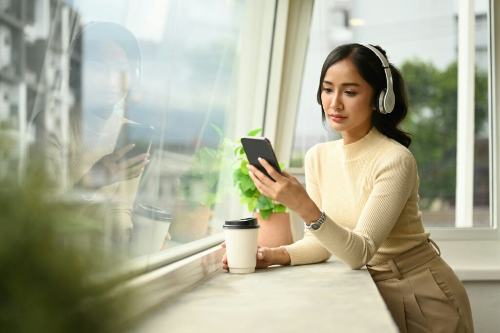 Pretty young woman in wireless headphone chatting with friends on mobile phone.