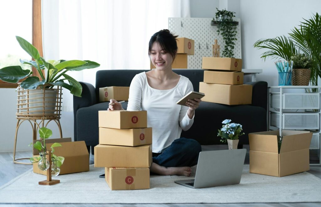Smiling young Asian business owner woman prepare parcel box and standing check online orders of