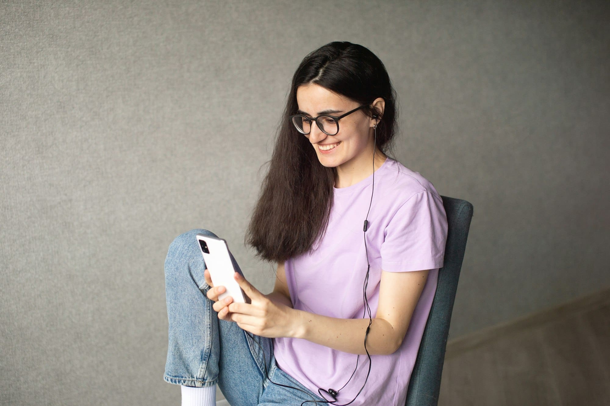 A young girl is sitting and looking at the phone with headphones